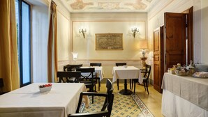Ein Esszimmer mit Tischen, Stühlen, einer Kandelaber und einem Gemälde an der Wand.