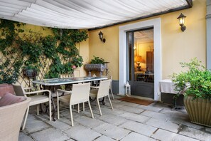 An outdoor patio with a table and chairs, a door leading to an interior space, and potted plants. - Room 'Villa Lombardi - Garden View' with Shared Pool, Garden, and Wi-Fi (Camaiore)