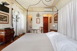 A hotel room with a large bed, wooden dresser, chandelier, and a view of the hallway. - Room 'Villa Lombardi - Garden View' with Shared Pool, Garden, and Wi-Fi (Camaiore)