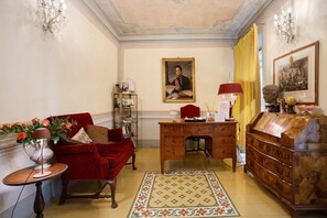 A room with a red armchair, a wooden desk, a bookshelf, a chandelier, and a patterned rug. - Room 'Villa Lombardi - Garden View' with Shared Pool, Garden, and Wi-Fi (Camaiore)