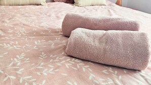 Een net opgemaakt bed met een roze bloemenbedekking, meerdere kussens, en een kleurrijk abstract schilderij aan de muur.