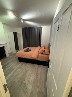 A bedroom with a bed, curtains, a door with a number, and a fireplace.