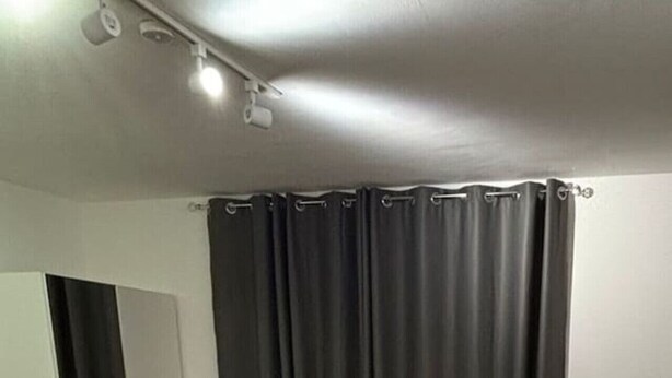 Un dormitorio con cama, cortinas oscuras, una puerta y una lámpara.