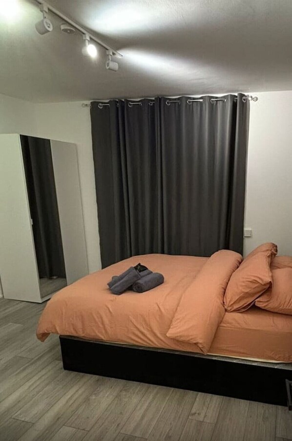 Une chambre à coucher avec un lit, des rideaux foncés, une porte et un luminaire.