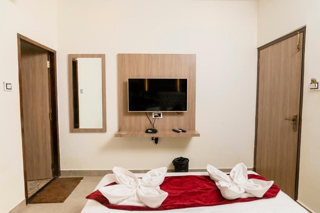 A hotel room with a bed, a TV mounted on the wall, a mirror, and two doors.