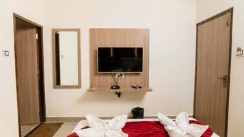 A hotel room with a bed, a TV mounted on the wall, a mirror, and two doors.