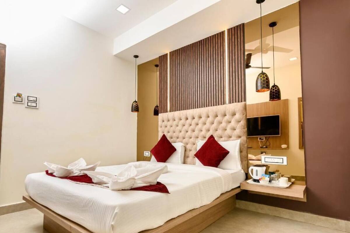 Quarto de hotel moderno com uma cama grande, televisão de tela plana e mesa de cabeceira de madeira.