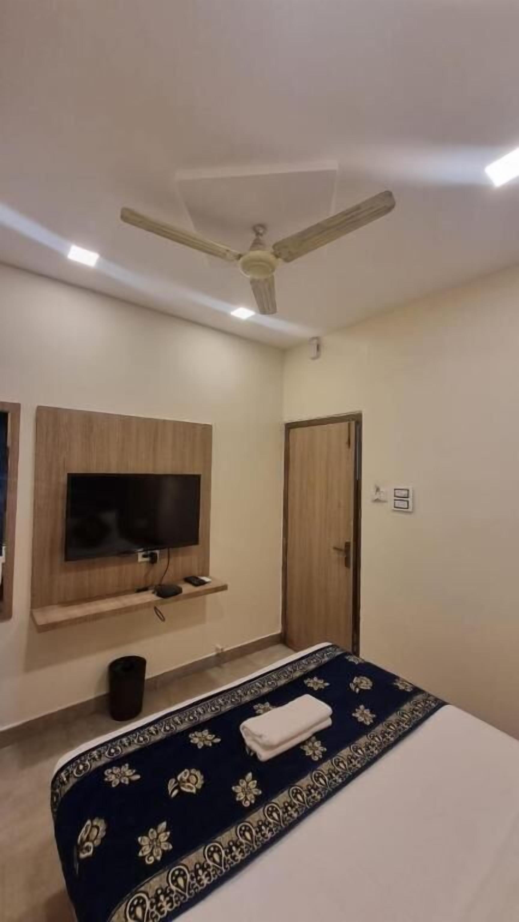 A bedroom with a bed, a television mounted on the wall, a ceiling fan, and a door.