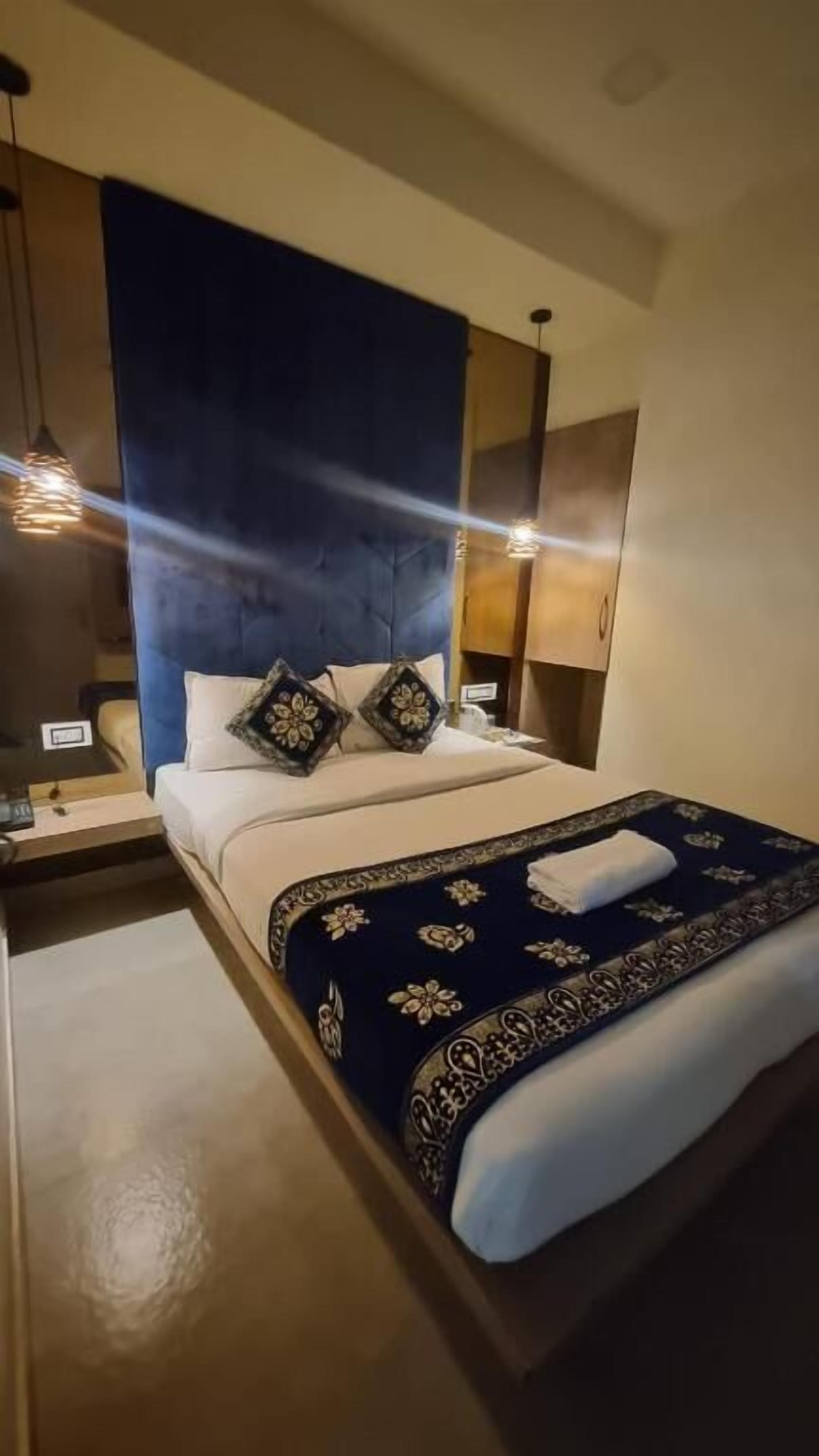 A hotel room with a bed, a nightstand, a lamp, and a blue accent wall.