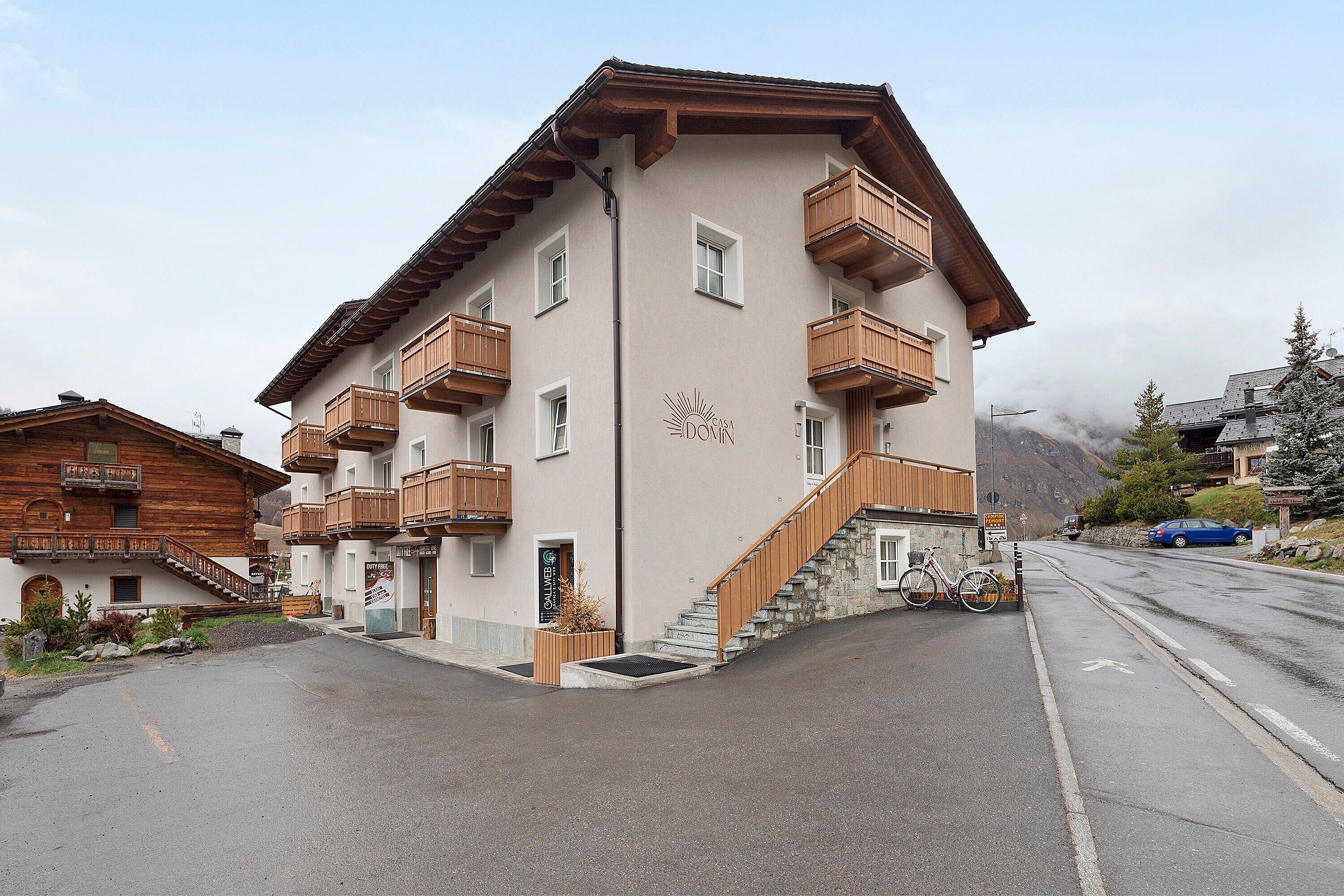 Un edificio a più piani con balconi in legno, una scala che conduce all'ingresso e un cielo sereno.