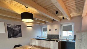 A modern kitchen with wooden beams, a dining area with a wooden table and chairs, and a window with a view. - Apartment '1 Trilocale' with Mountain View, Balcony and Wi-Fi (Livigno)