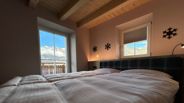 A bedroom with a large bed, a window with a view of mountains, and a ceiling with wooden beams. - Apartment '1 Trilocale' with Mountain View, Balcony and Wi-Fi (Livigno)