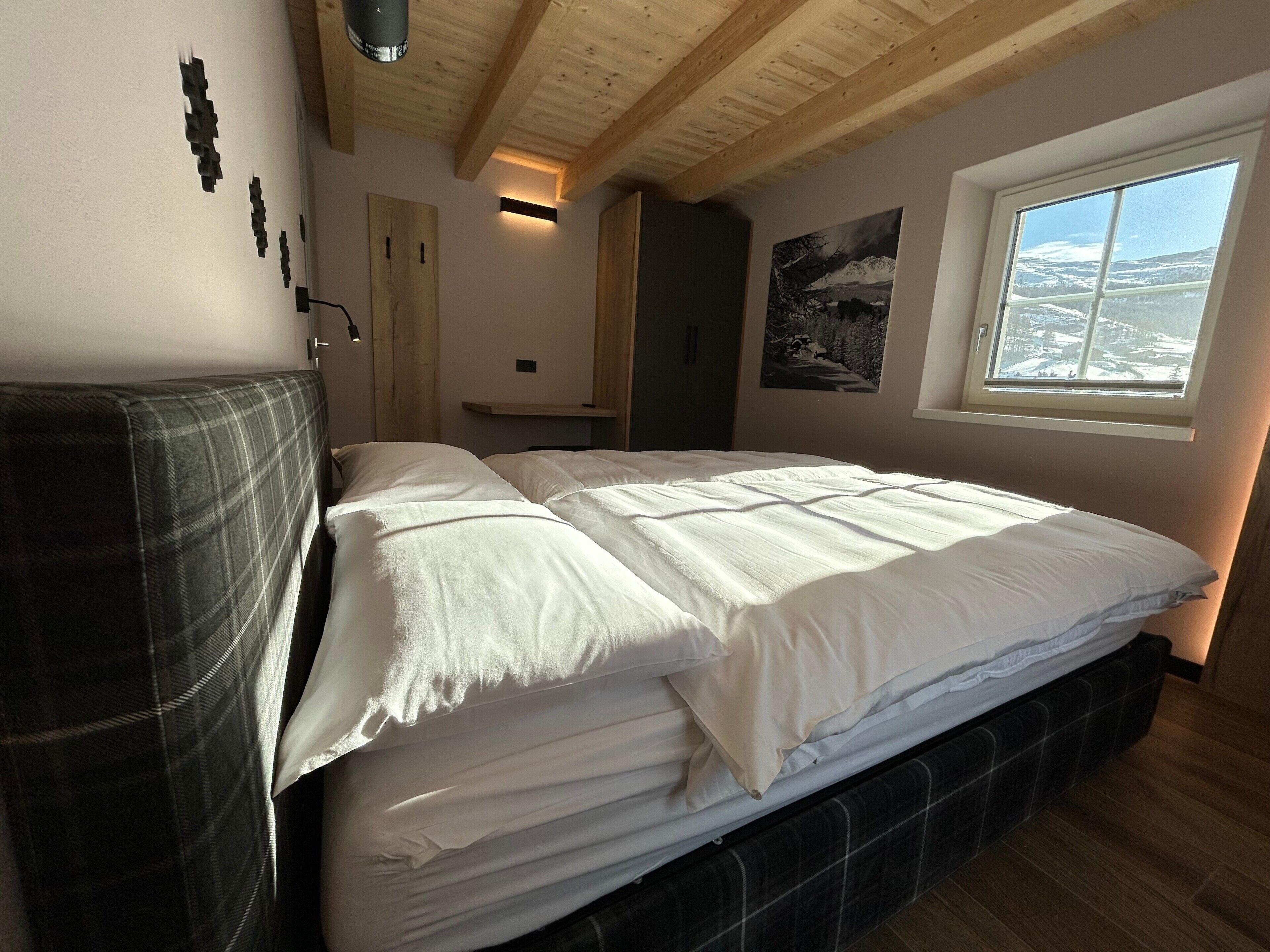 Un dormitorio con una cama, un ventanal y una puerta, además de una lámpara fijada a la pared.