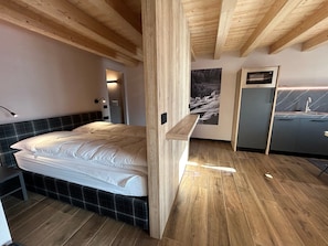 A bedroom with a bed, a nightstand, a wooden bench, a wall-mounted shelf, a painting, and a built-in cabinet. - Studio '2 Monolocale' with Mountain View, Balcony and Wi-Fi (Livigno)