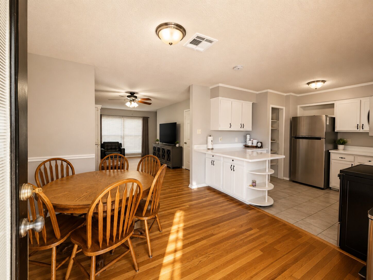 A modern kitchen with white cabinets, a stainless steel refrigerator, and a dining area with wooden chairs and a table.