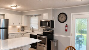 Una cocina moderna con armarios blancos, electrodomésticos de acero inoxidable, un microondas y un reloj en la pared.