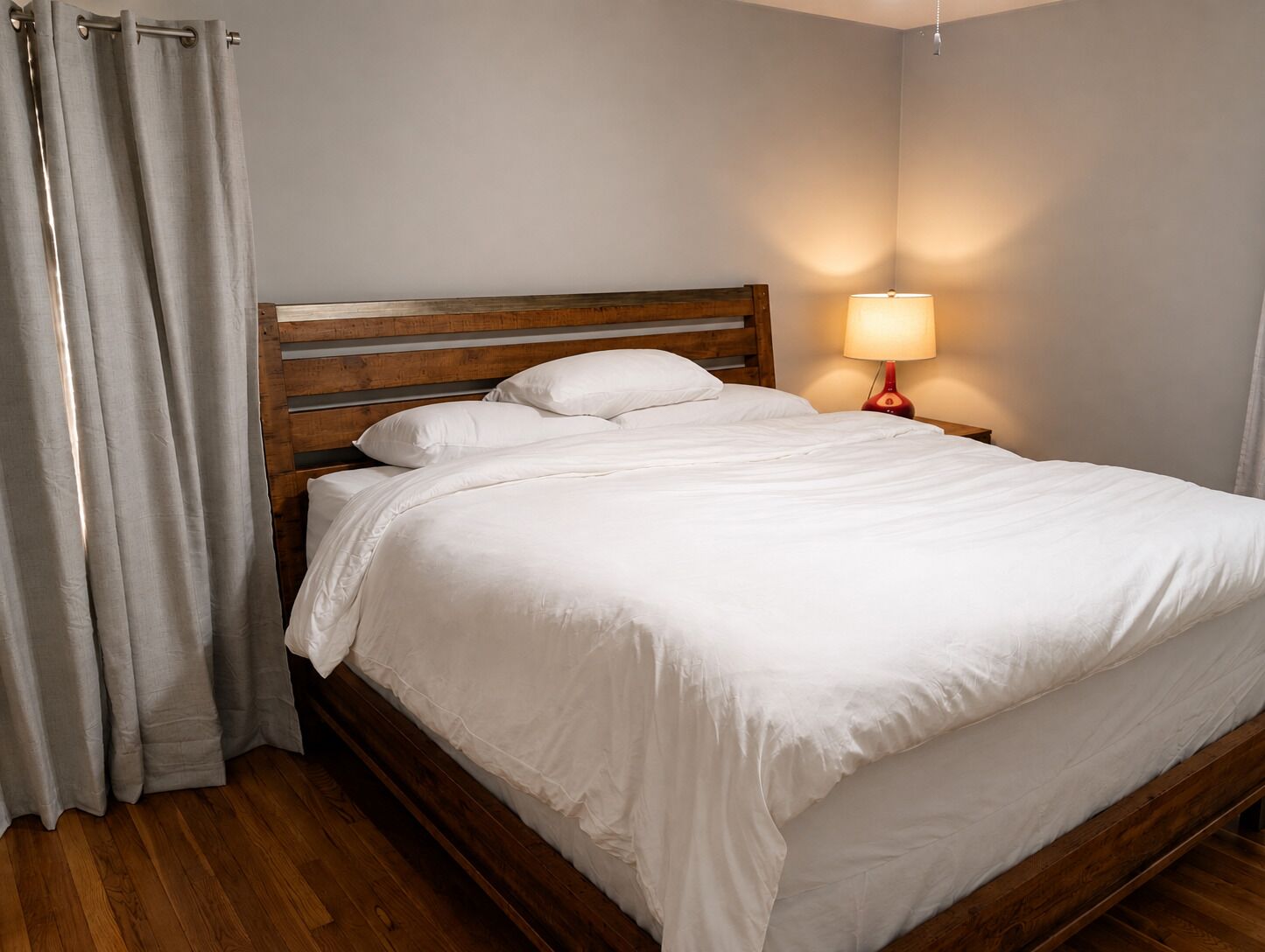 A neatly made bed with white linens, a wooden headboard, and a bedside lamp.