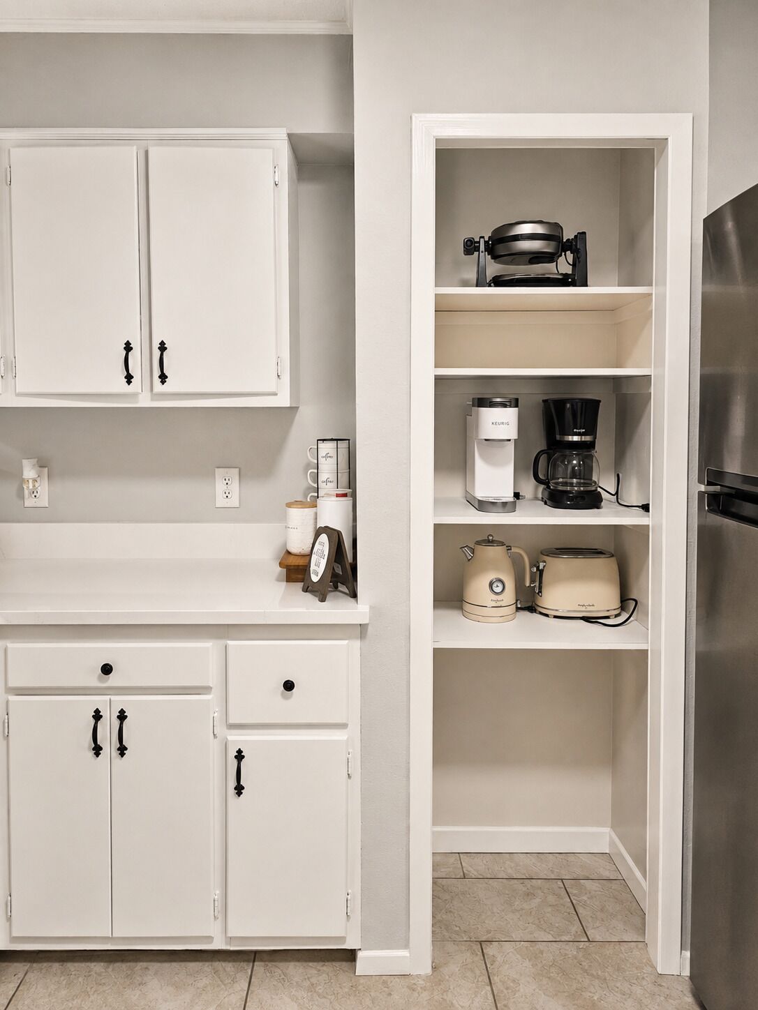 A kitchen with white cabinetry, a coffee maker, a toaster, and a kettle.