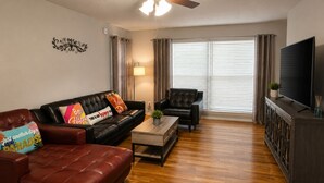 Una sala de estar con sofá, sillón, mesa de centro y televisor sobre un mueble.