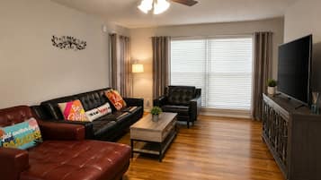 A living room with a sofa, armchair, coffee table, and a TV on a cabinet.
