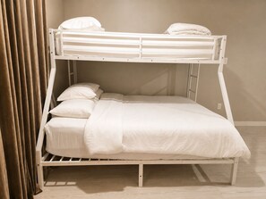 Een stapelbed met witte lakens, een houten frame en een gordijn dat gedeeltelijk is dichtgeschoven.