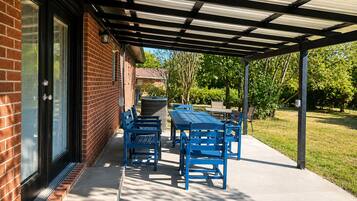 A covered patio area with a brick building, outdoor furniture, and a clear view of the surrounding greenery.