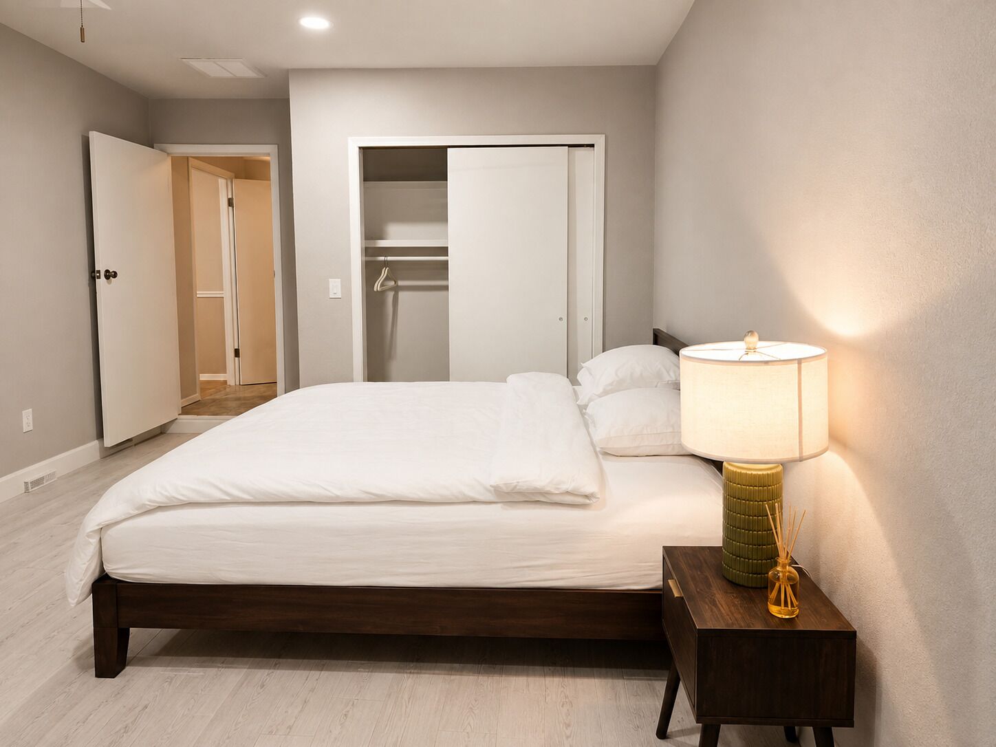 Quarto com cama, abajur e armário com a porta aberta.