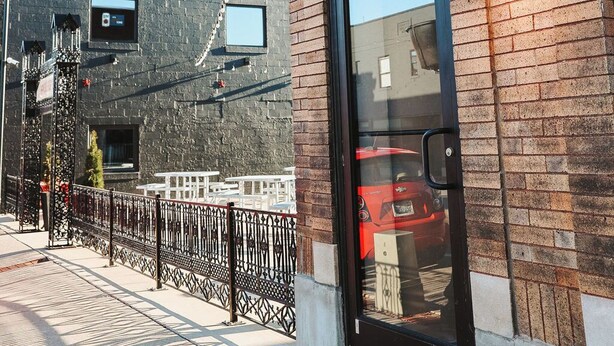 Un edificio de ladrillo con un amplio escaparate de vidrio, una ventana pequeña y una cerca de metal.