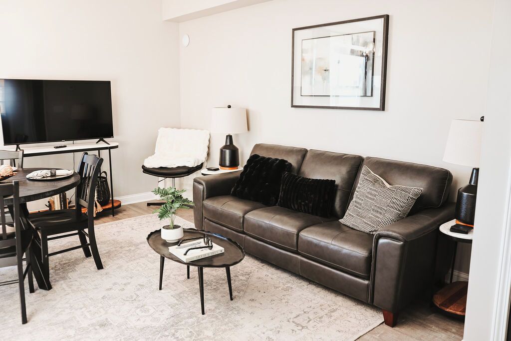 A living room with a brown leather sofa, a flat-screen TV, a dining table with chairs, a coffee table, and a framed picture on the wall.