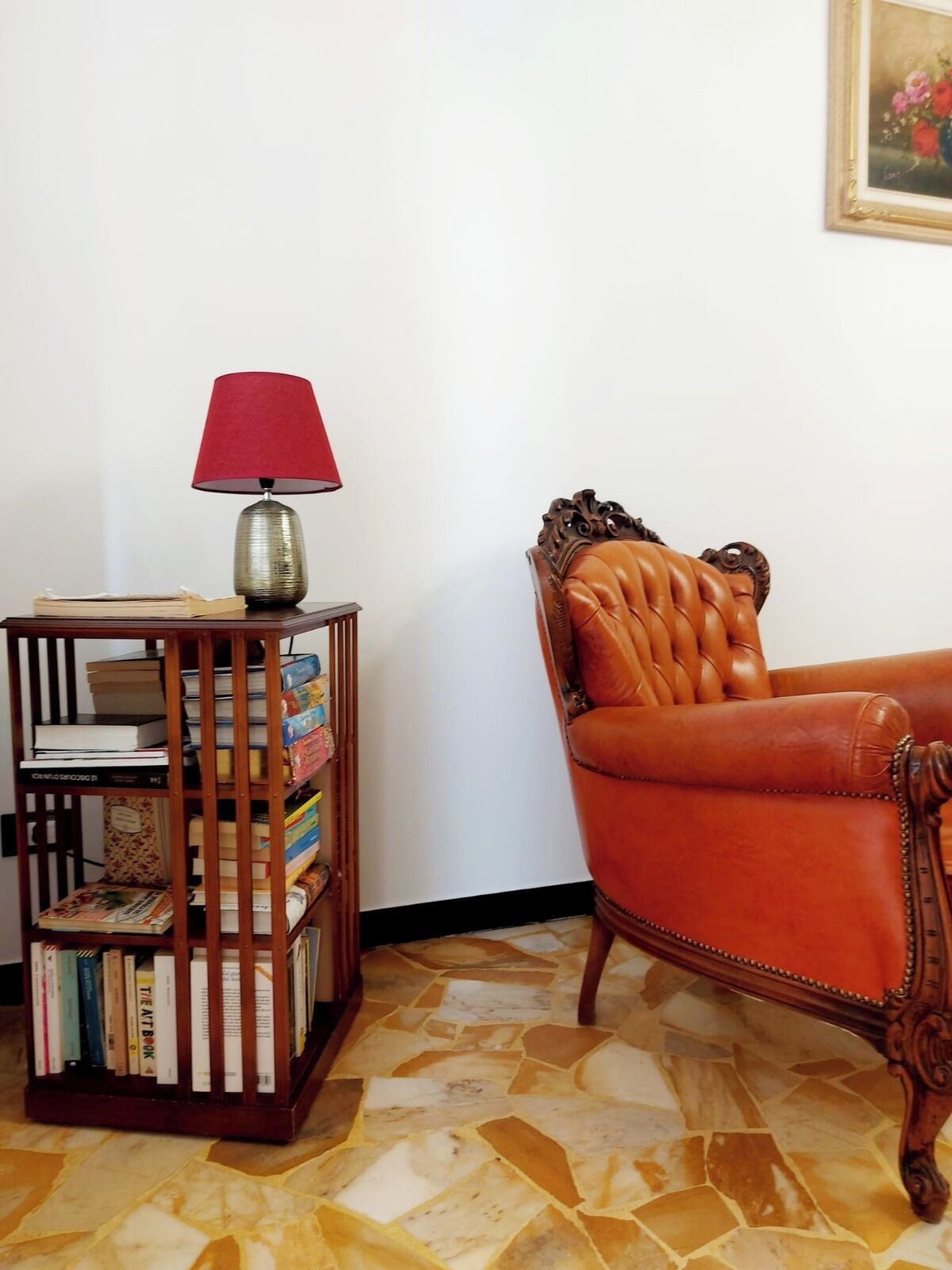 A room with a wooden bookshelf, a red lamp, a leather armchair, and a tiled floor.