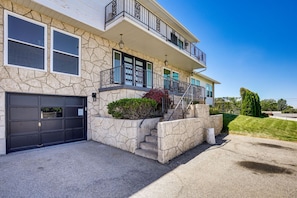 A two-story house with a stone facade, a black garage door, and a small front yard with a staircase leading to a balcony.