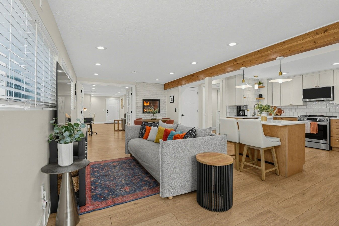 A modern kitchen with a central island, a dining area with white chairs, and a living room with a grey sofa.