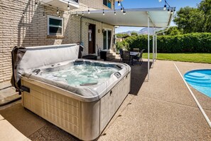 Un jacuzzi en un espacio exterior cubierto, con piscina y mobiliario de patio.