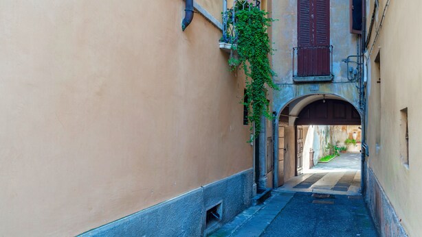 A narrow alleyway with a building on one side and an archway leading to another structure. - Suite Cavour (Brescia)