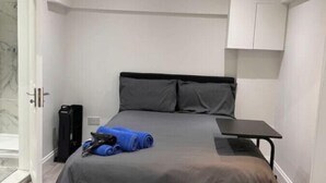 A modern bedroom with a bed, a small table, and a suitcase. - Central London, Zone 2, Studio Flat (Greater London)