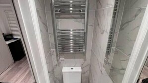 A narrow bathroom with a toilet, a sink, and a shower. - Central London, Zone 2, Studio Flat (Greater London)