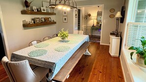 A dining area with a long table, chairs, a bench, wooden flooring, wall shelves, and a hanging light fixture. - Masters Rental 3.5 miles from the Augusta National (Martinez)