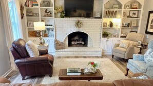 A living room with a fireplace, leather sofas, a coffee table with books, and a TV mounted above the fireplace. - Masters Rental 3.5 miles from the Augusta National (Martinez)