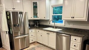 A kitchen with white cabinets, stainless steel appliances, a granite countertop, and a window with a view of trees. - Masters Rental 3.5 miles from the Augusta National (Martinez)