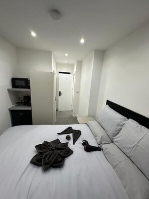 A hotel room with a bed, a microwave, a small desk, and a door leading to another room.