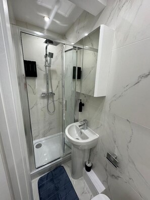 A modern bathroom with a glass-enclosed shower, a pedestal sink, and a marble-tiled wall. - Central London Zone 1 Room wbath (Greater London)