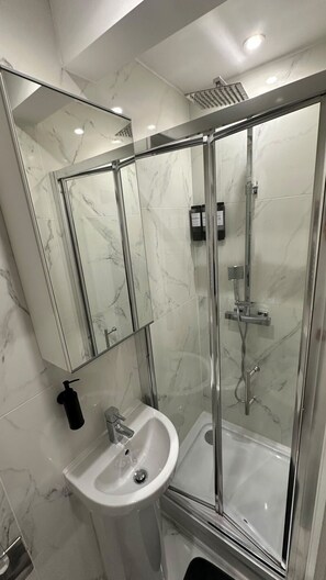 Un baño moderno con ducha envuelta en vidrio, un lavabo blanco y un espejo grande.