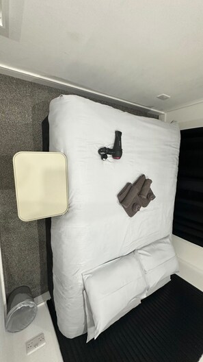 A compact bed with a pillow, a small bedside table, and a wall-mounted lamp. - London Kings Cross Room w Bath (Greater London)