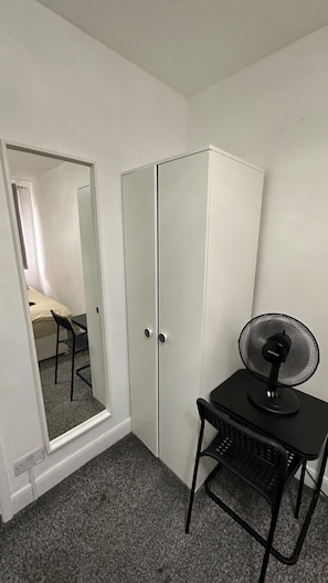 A small room with a wardrobe, a chair, a desk, and a standing fan. - Close to Oxford street studio (Greater London)