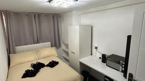 Habitación de hotel con una cama, un escritorio con microondas, un armario y un pequeño bote de basura.