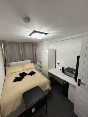 A hotel room with a bed, a desk with a microwave, a wardrobe, and a small trash bin. - Marylebone Room + bathroom (Greater London)