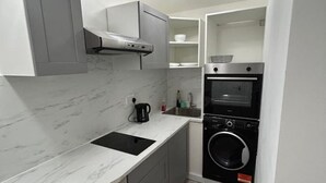 Una cocina compacta con horno integrado, lavadora y cubo de basura.