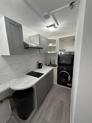 A compact kitchen with a built-in oven, a washing machine, and a trash bin. - Marylebone Room + bathroom (Greater London)