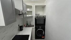 Une cuisine compacte équipée d’un four encastré, d’un lave-linge et d’une machine à café posée sur le plan de travail.