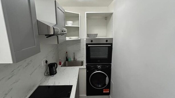 Una cocina compacta con horno integrado, lavadora y cafetera sobre la encimera.